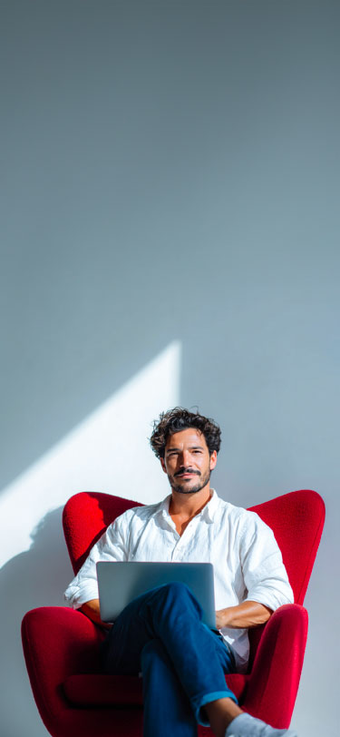 Hombre joven sonriente sentado en una silla con un computador sobre las piernas