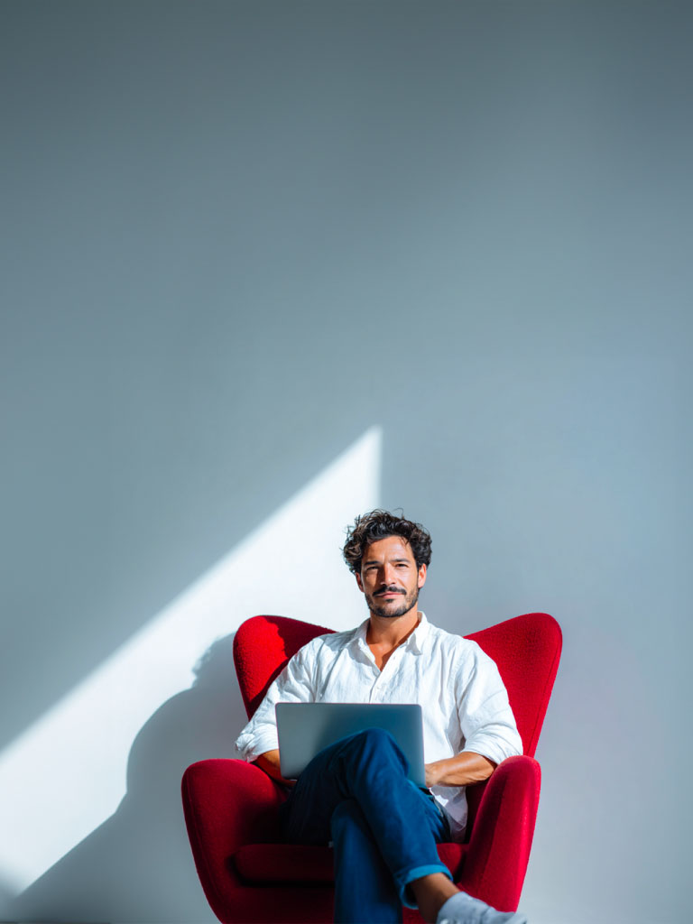 Hombre joven sonriente sentado en una silla con un computador sobre las piernas