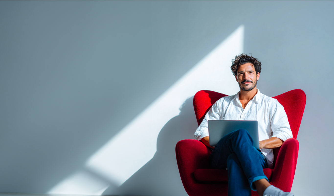 Hombre joven sonriente sentado en una silla con un computador sobre las piernas